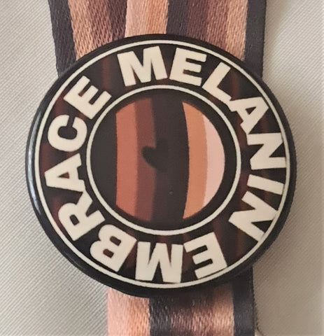 38mm round badge with the worlds Embrace Melanin  around the Embrace globe colours with a black heart in the middle. 
