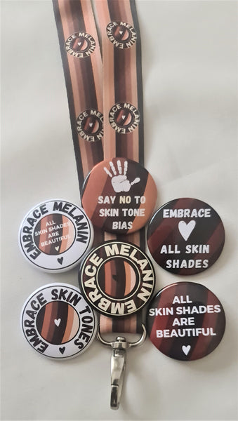 Six 38mm round badges on an Embrace Melanin lanyard. One Embrace Shades globe colours in the background with all skin shades are beautiful. and a heart. One Embrace all skin shades with a heart, one handprint and, say no to skin tone bias, one with Embrace skin tones around the Embrace Shades globe with a heart. One with Embrace Melanin and the Embrace shades globe and a heart and one Embrace Melanin around the Embrace shades globe with, all skin shades are beautiful,